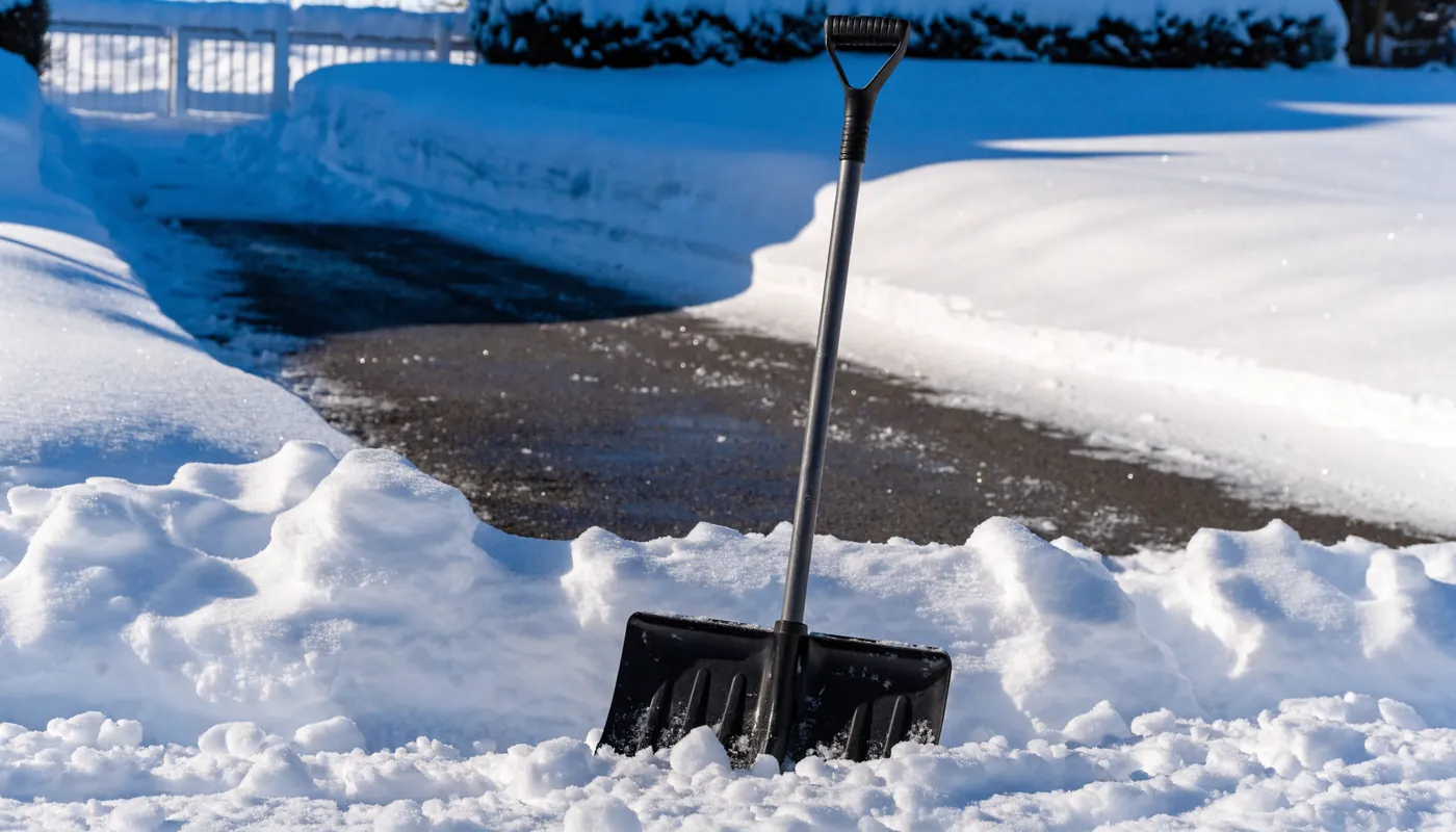 Schneeschaufel in frischem Schnee neben geräumter Einfahrt
